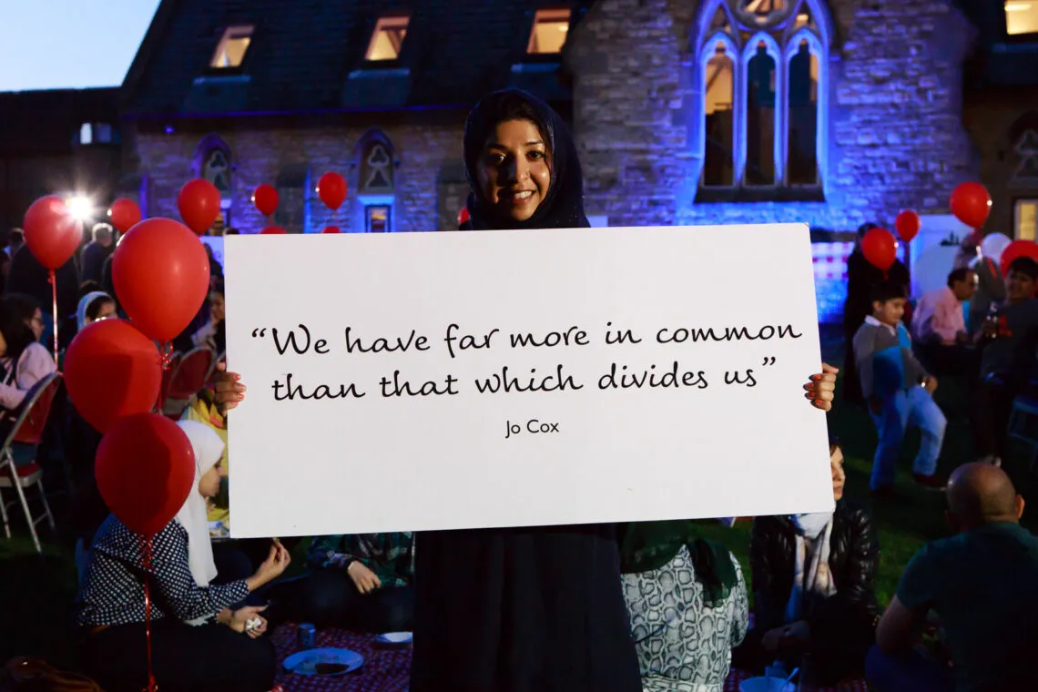 Photo of person at a Great Get Together event with a sign that says "We have far more in common than that which divides us" Jo Cox